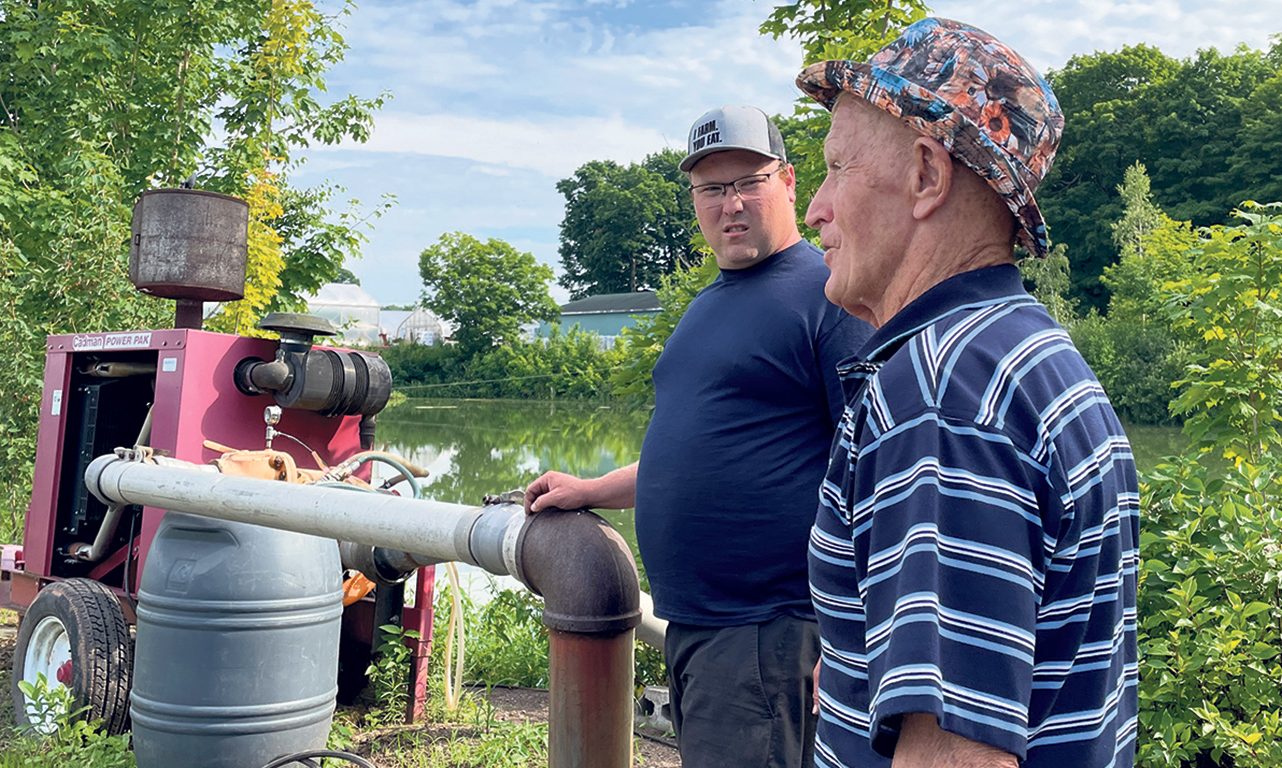 Marc-André et son grand-père Roland Gosselin avec le moteur et la pompe attachés au système d’irrigation.