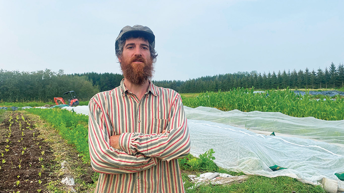 Antoine Boissé-Gadoury devant l’un des champs de la Coop la Hutte, où il cultive une trentaine de variétés de fruits et de légumes. Photos : Émilie Parent-Bouchard