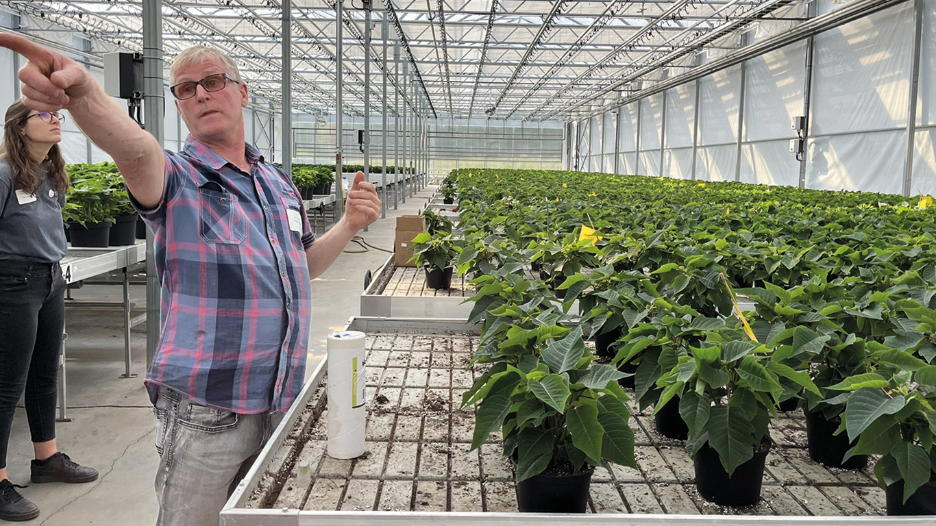 Michel Grégoire explique aux visiteurs que la température est captée par une boîte qui se situe à mi-hauteur du plafond de la première serre et qu’elle envoie une commande au système automatisé pour ajuster le chauffage en temps réel. Photos : Myriam Laplante El Haïli/TCN